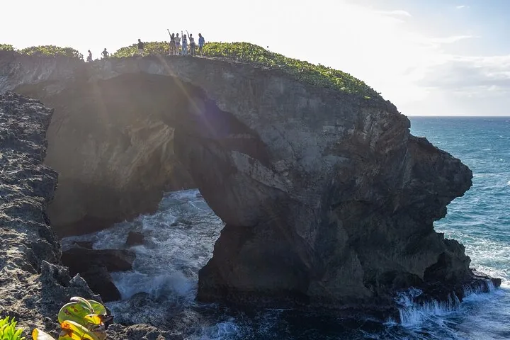 Personas en silueta de pie sobre un puente de roca natural sobre agua de mar agitada.