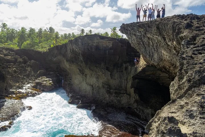 Grupo de personas saludando desde un acantilado alto sobre una cala rocosa y turbulenta.