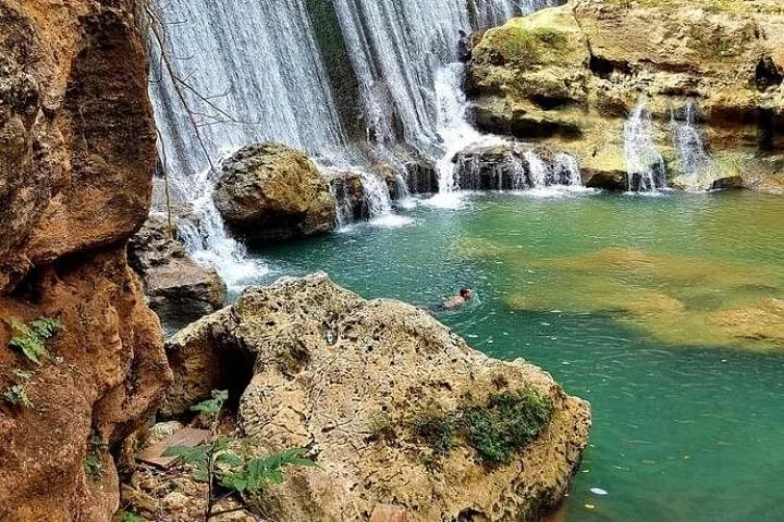 Person, die in einem Becken am Fuß eines felsigen Wasserfalls schwimmt.