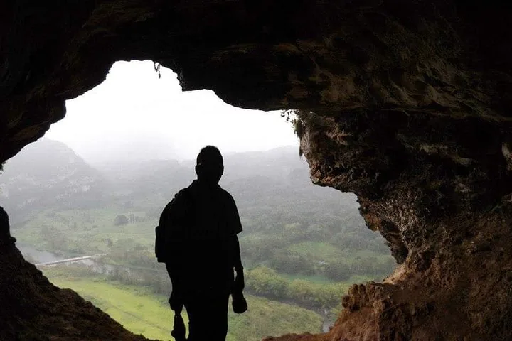 Silhouette einer Person in der Cueva Ventana, die auf ein nebliges Tal hinausblickt.